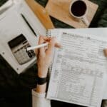 Person reviewing documents with calculator and laptop